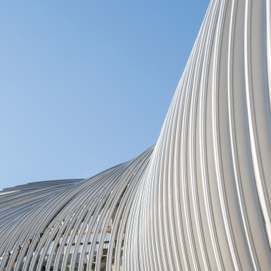 Detail view of the perforated metal scrim. The curve profile of the metal scrim at each bridge section was digitally generated and tested to reach a pleasing form that would meet the function requirements, and within the physical parameter of standard standing seam metal panels.   
Photo by Michael Muraz.