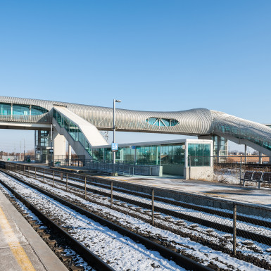 View of the bridge from the train platform. Design considerations were made to balance formal aesthetics with maximizing views for the pedestrians minimizing possible distractions to drivers (from either material glare or pedestrians), functional openings for stairs, and material bending limitations of metal panels. Photo by Michael Muraz.